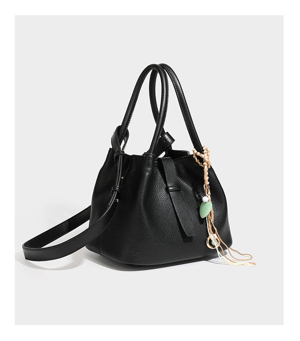Pebbled leather-look bucket tote bag with rolled double handles, drawstring closure, braided cord charm, and detachable