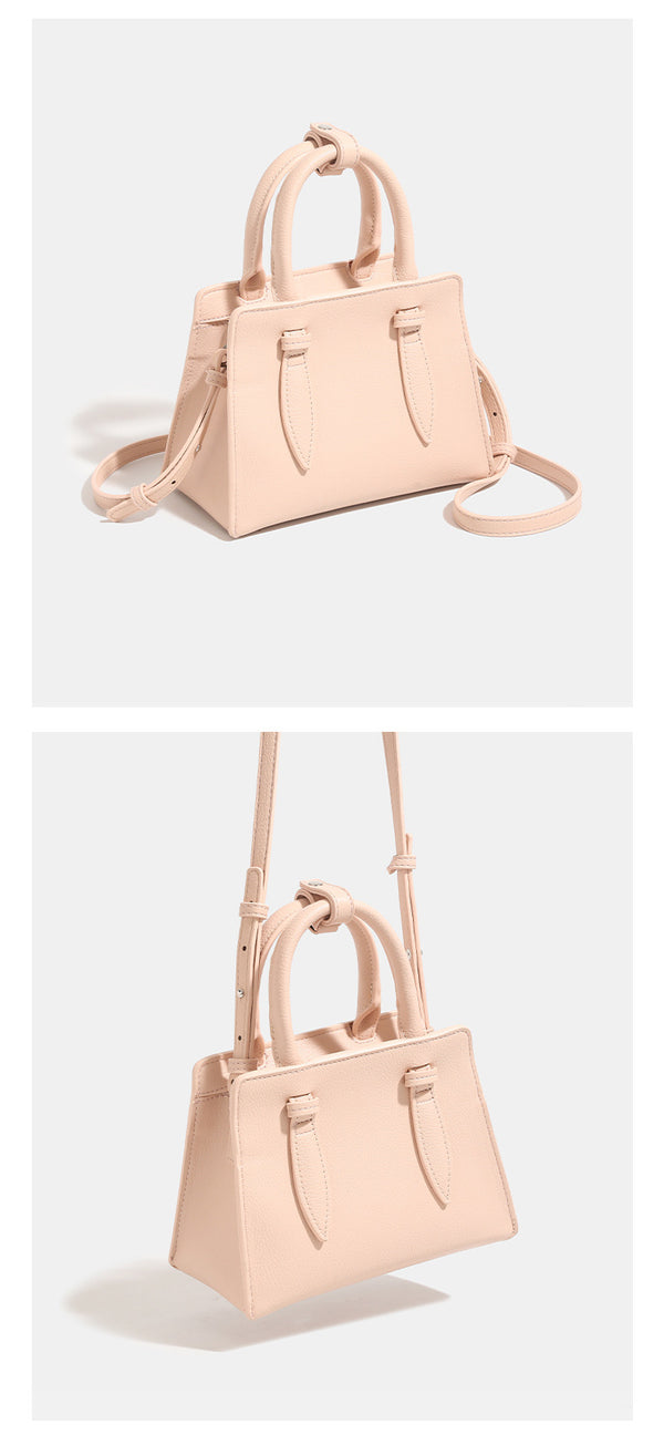 Small structured trapezoid top-handle bag in pebbled matte finish with decorative strap tabs, twin knotted handles, and