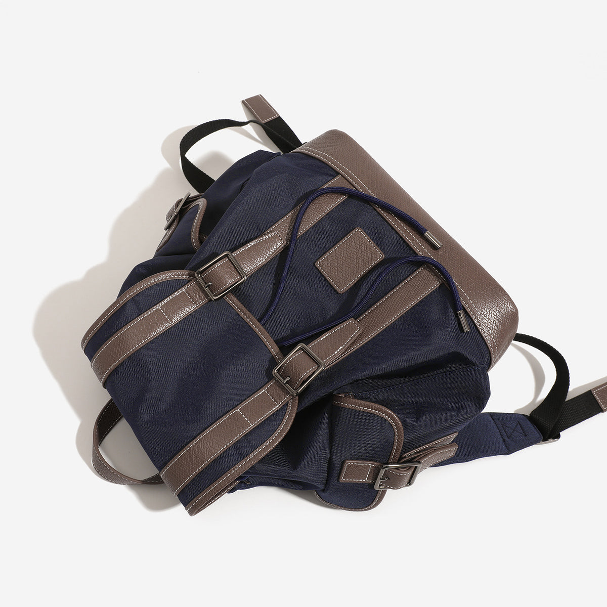 Deep navy canvas backpack with brown textured leather-look trim, drawstring flap closure, buckle-strap front detail, and