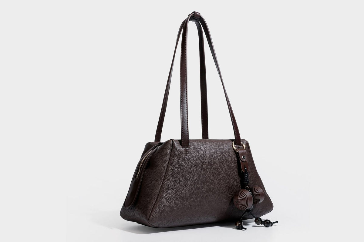 Structured trapezoid shoulder bag in dark brown pebbled leather-look finish with slim double straps, top zip closure, side