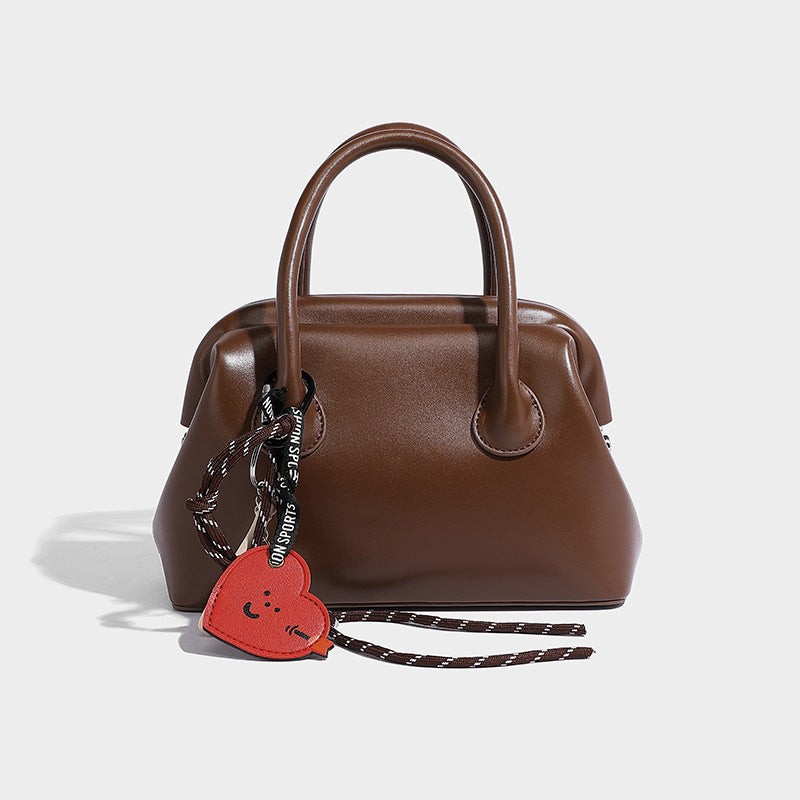 Small structured shell top-handle bag in red with heart charm and braided cord detail, smooth leather-look finish, detail
