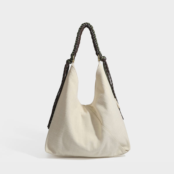 Soft slouchy cream canvas shoulder tote with braided brown and green cord handle, gold-tone ring hardware, and tassel trim