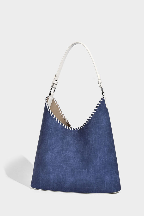 Denim-blue hobo tote with white leather-look shoulder strap, contrast whipstitch trim along curved open top, and silver-tone