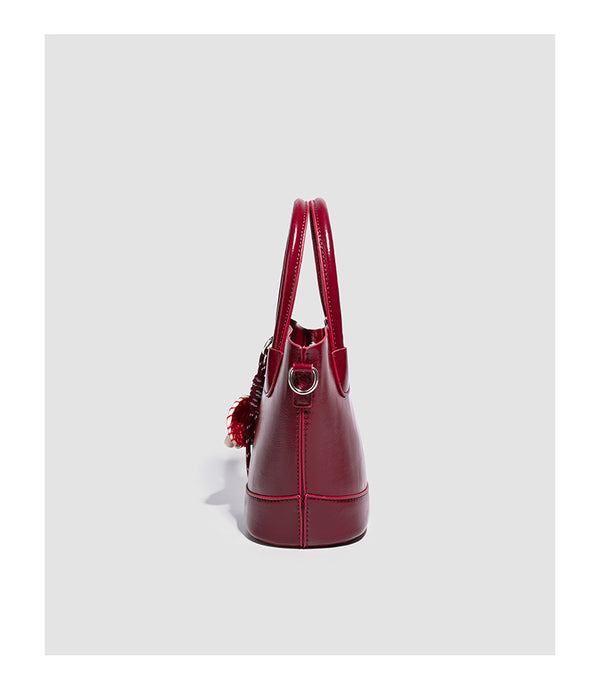 Glänzende, strukturierte Beuteltasche in Burgunderrot mit zwei abgerundeten Tragegriffen, silberfarbenen Beschlägen, dekorativem Anhänger und