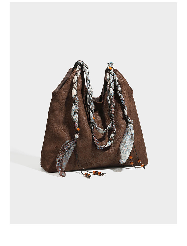 Slouchy paisley-embossed suede-look shoulder tote bag with braided patterned fabric straps and wood bead accents, detail view