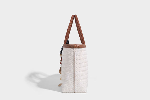 Structured woven-texture tote bag with brown braided top handles, decorative tassel charm, and detachable shoulder strap
