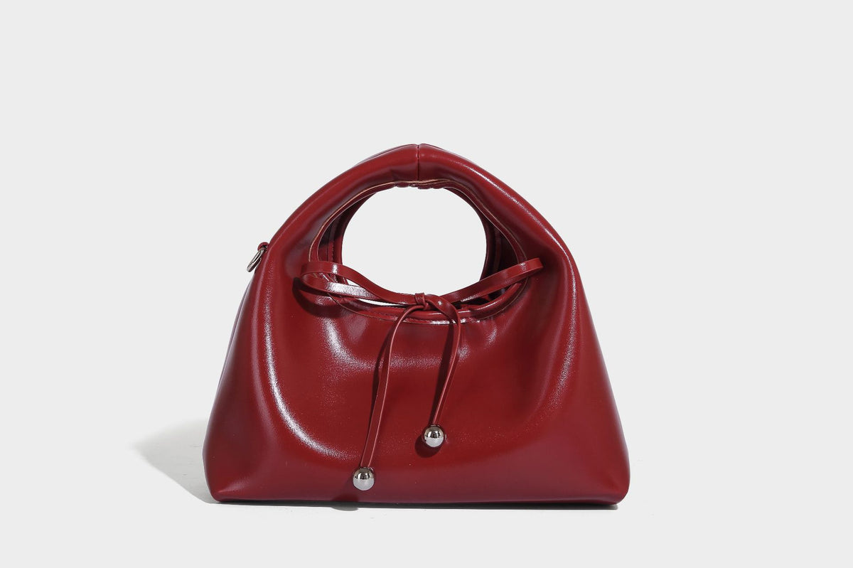 Kleine kuppelförmige Henkeltasche in glänzender Lederoptik mit Kordelzugverschluss, weißem Spitzen-Schleifenanhänger und silberfarbenen Metallbeschlägen