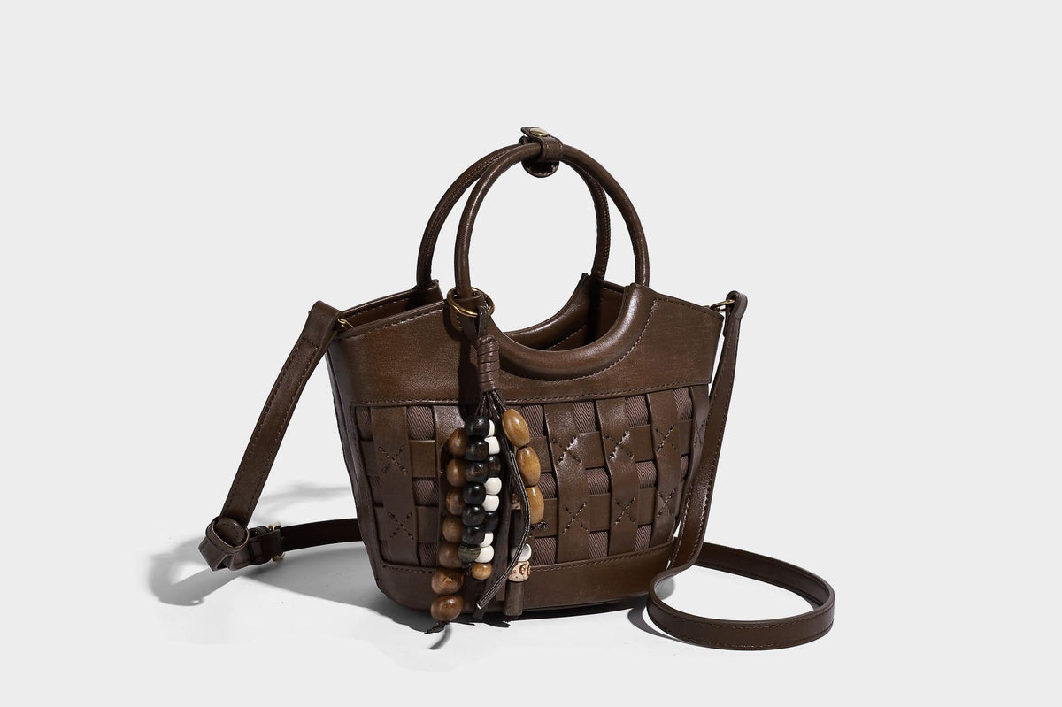 Small woven-panel bucket bag with circular ring handles, beaded tassel charm, and detachable crossbody strap in brown, detail