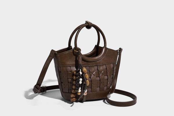 Small woven-panel bucket bag with circular ring handles, beaded tassel charm, and detachable crossbody strap in brown, detail