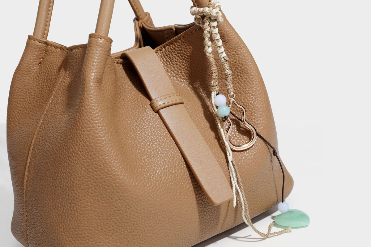 Pebbled leather-look bucket tote bag with rolled double handles, drawstring closure, braided cord charm, and detachable