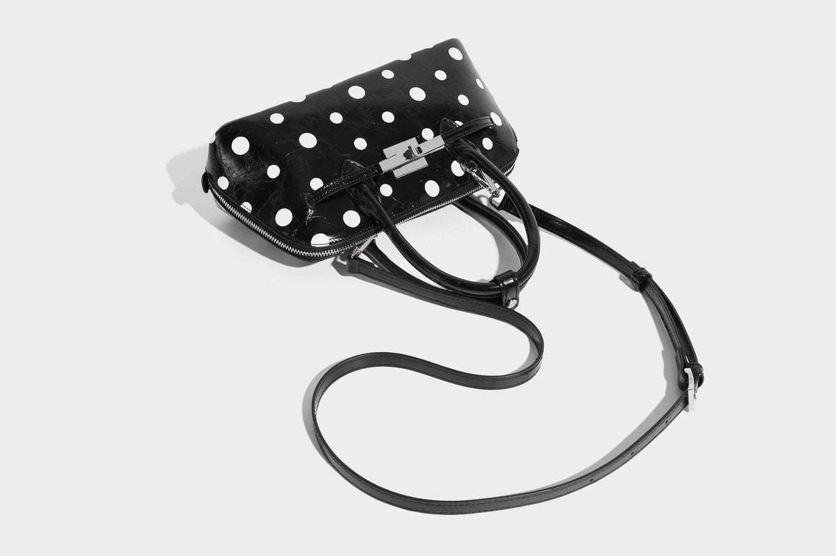 Glossy structured polka-dot satchel bag with dual top handles, silver turn-lock hardware, and detachable shoulder strap