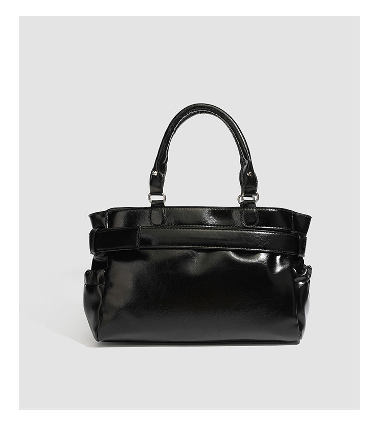 Black glossy structured tote bag with rivet and buckle detail, dual top handles, and detachable shoulder strap, detail view