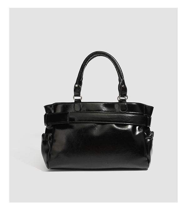 Black glossy structured tote bag with rivet and buckle detail, dual top handles, and detachable shoulder strap, detail view