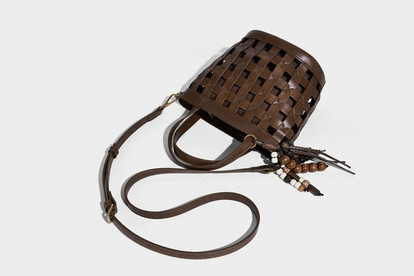 Small woven lattice bucket bag in brown leather-look finish with beaded tassel charm, dual top handles, and detachable