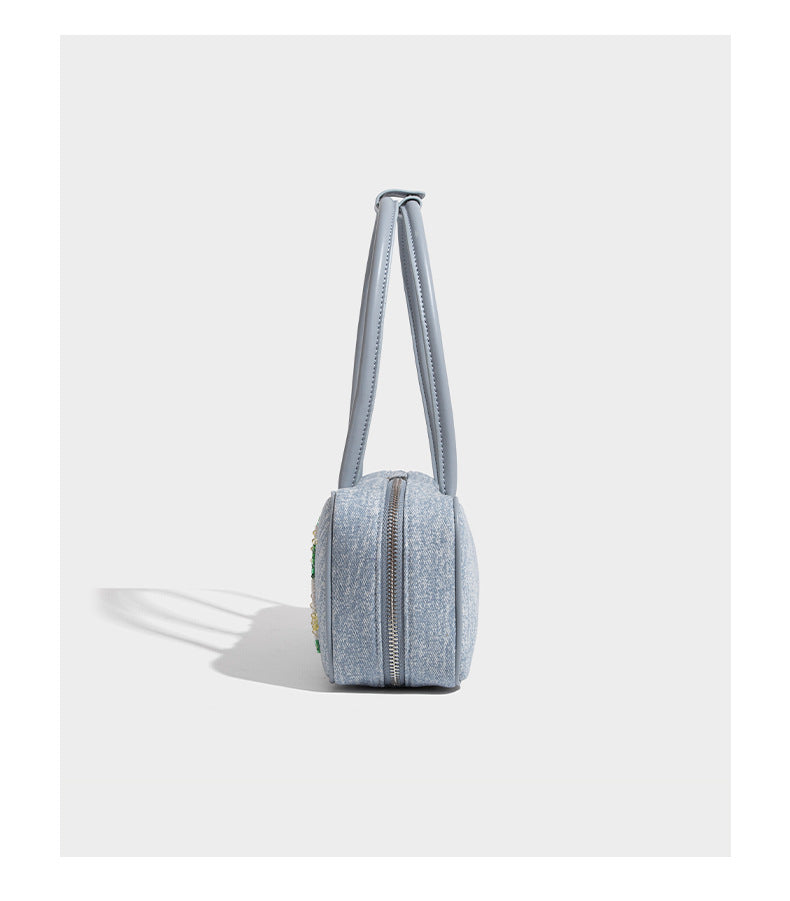 Small structured light blue denim-texture bowling bag with white floral bead embroidery, dual rounded top handles, and
