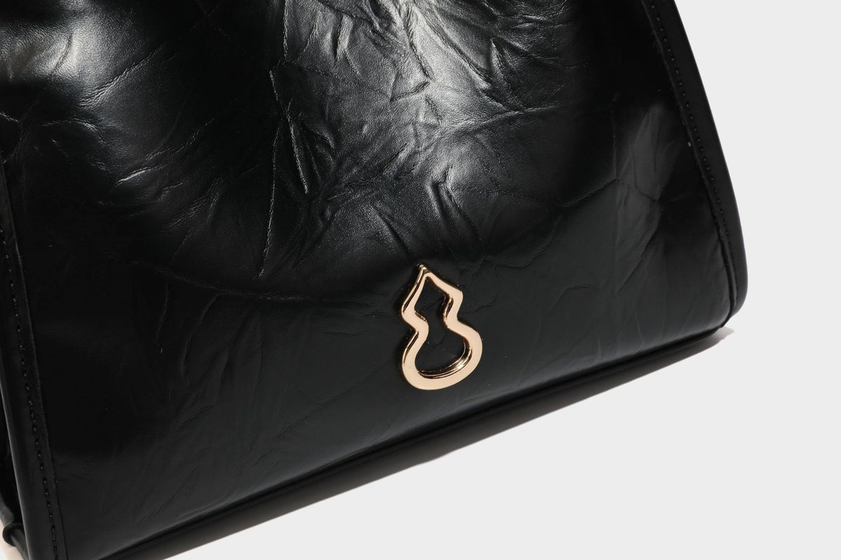 Strukturierte, trapezförmige Schultertasche aus glänzender, geknautscht wirkender Lederoptik mit goldfarbenen Beschlägen auf der Vorderseite und langem, verstellbarem