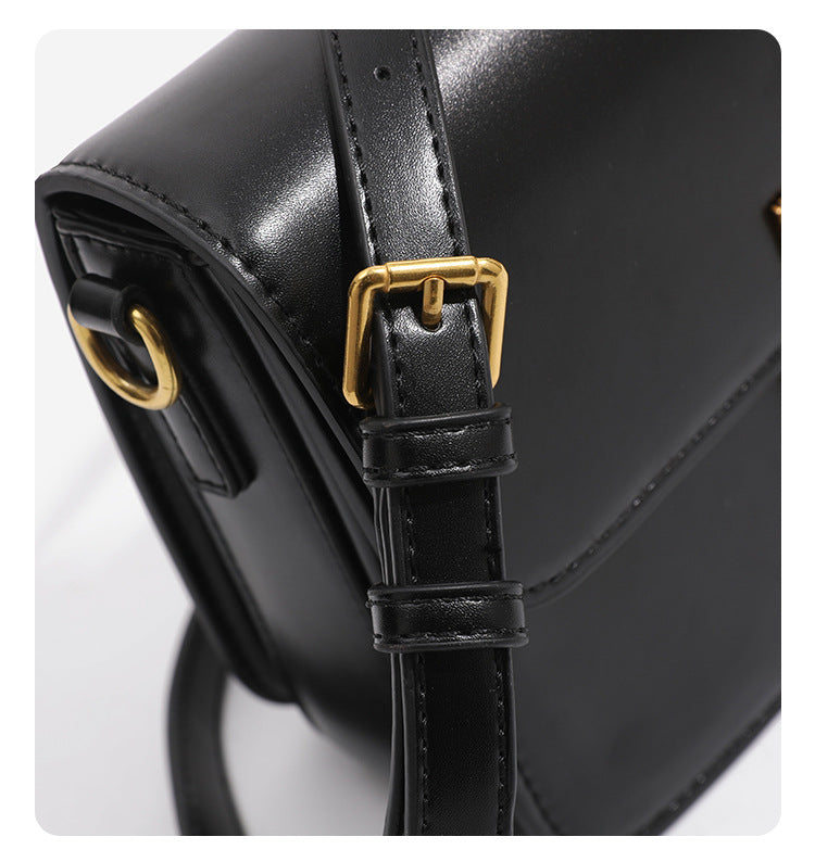 Mini structured black flap crossbody bag with gold-tone ribbed rectangular clasp and adjustable shoulder strap, detail view