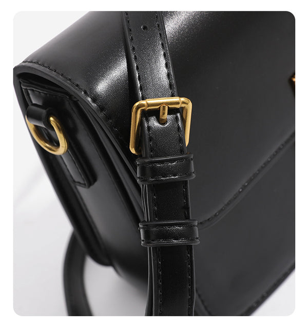 Mini structured black flap crossbody bag with gold-tone ribbed rectangular clasp and adjustable shoulder strap, detail view