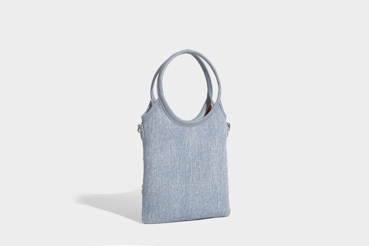 Kleine hellblaue Mini-Tote-Bag aus Stoff mit weißer Perlenblumenverzierung, runden Henkeln, silberfarbenen Beschlägen und