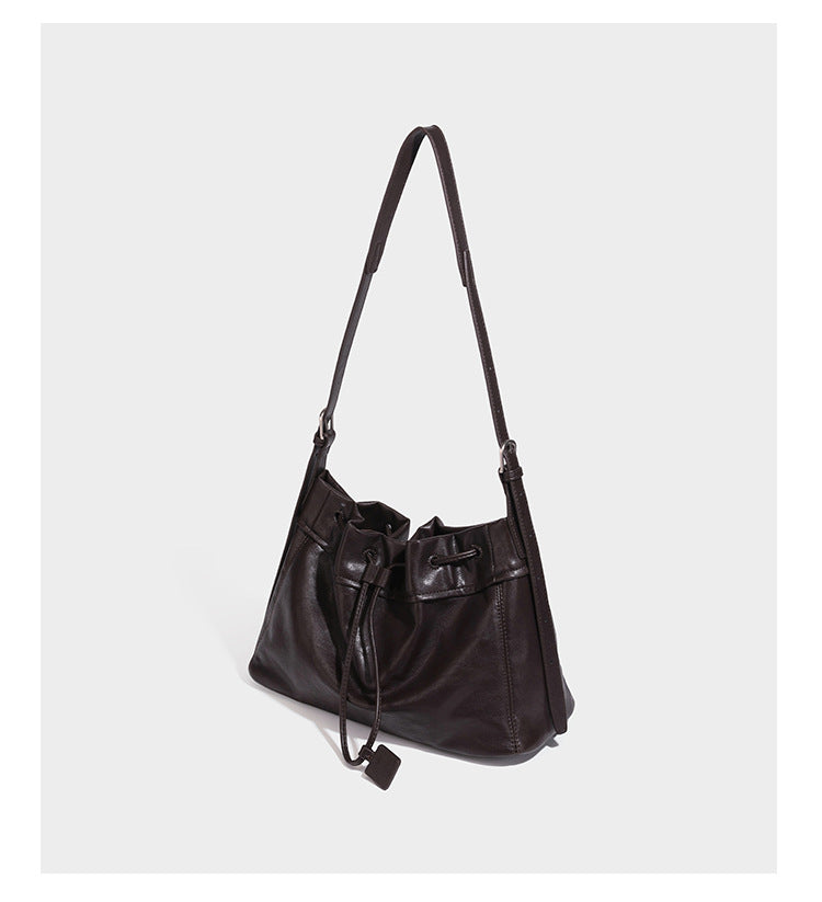 Slouchy drawstring bucket bag in dark brown leather-look finish with long adjustable shoulder strap and gathered tie closure