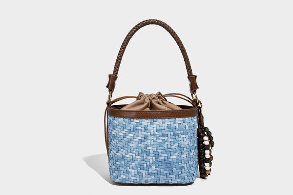 Small light blue woven bucket bag with brown leather-look trim, braided top handle, brass-tone ring hardware, drawstring