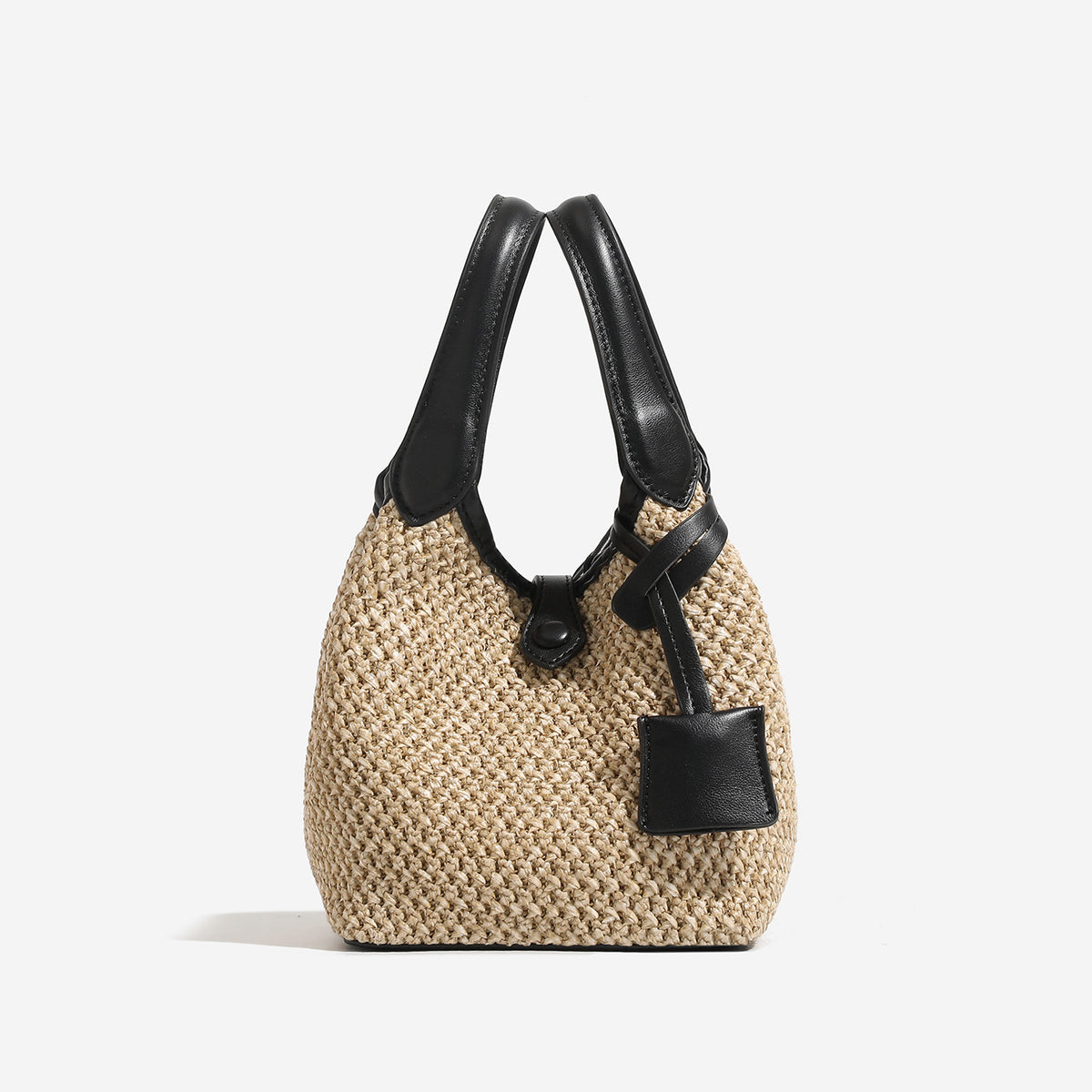 Woven beige straw bucket bag with black leather-look trim, dual top handles, detachable shoulder strap, and front snap