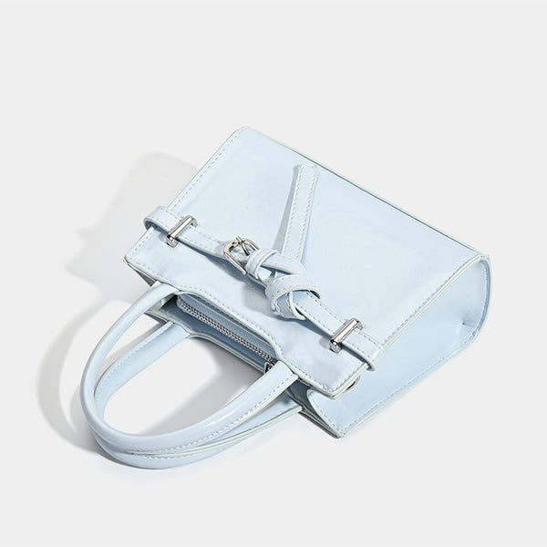 Small structured trapezoid mini top-handle bag with front belt-knot buckle detail and glossy leather-look finish, detail view