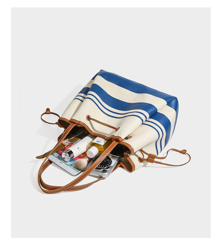 Large cream and navy striped canvas bucket tote bag with tan leather-look trim, drawstring closure, and double shoulder