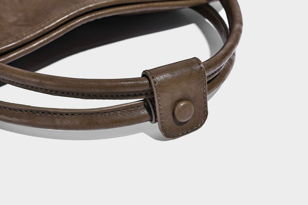 Glänzende Tragetasche in geknautschtem Lederlook mit geprägtem kreisförmigem Emblem, Quastenverschluss, zwei Tragegriffen und abnehmbarem