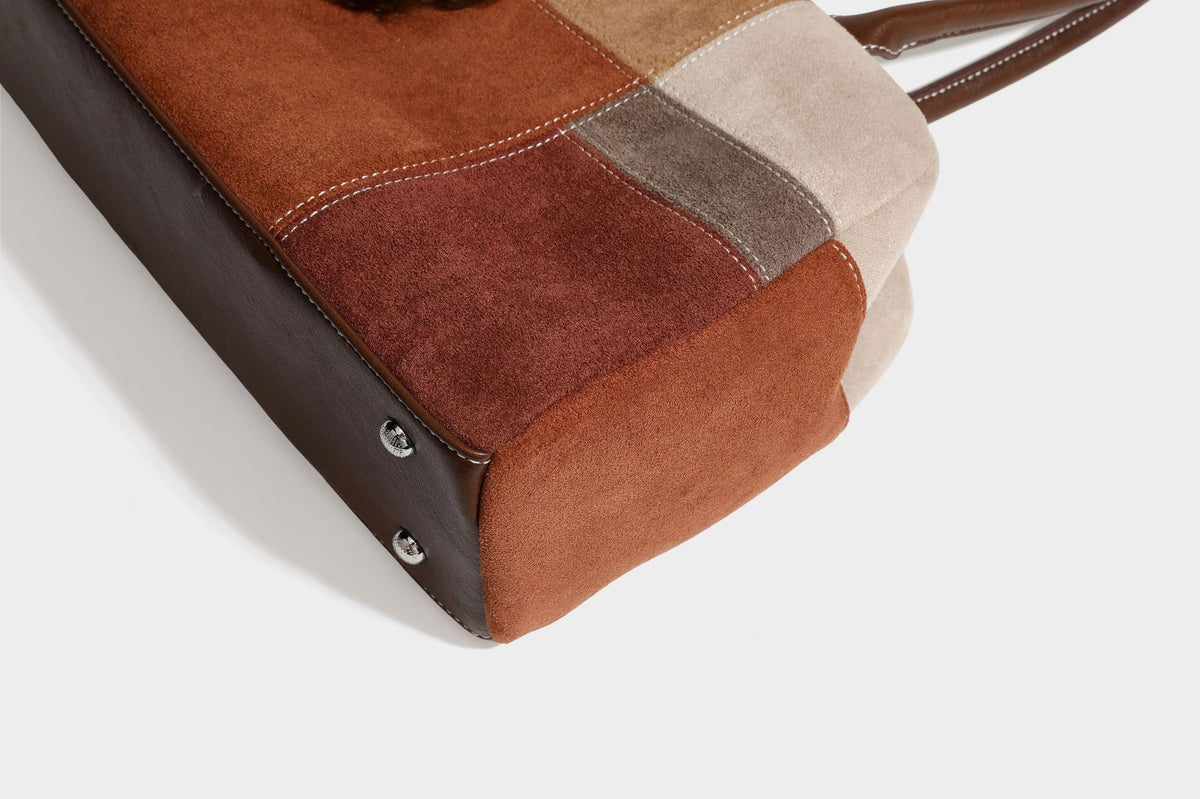 Boxy patchwork suede-look shoulder tote in tan, beige, rust, and brown panels with double brown straps and hanging doll