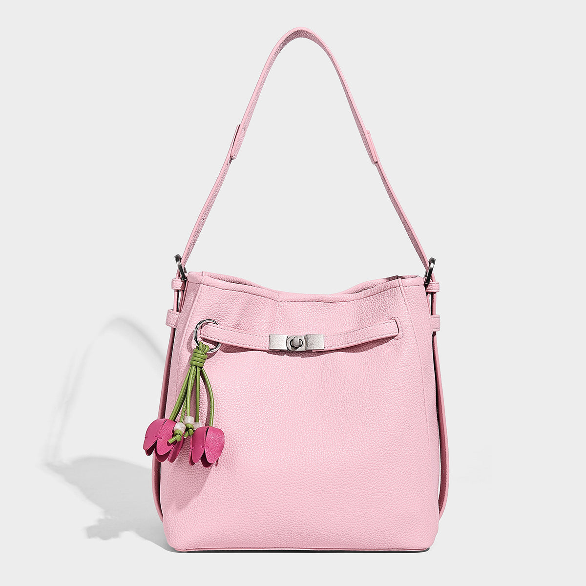 Soft-structured pebbled bucket shoulder bag with front turn-lock strap detail, adjustable strap, and hanging floral tassel