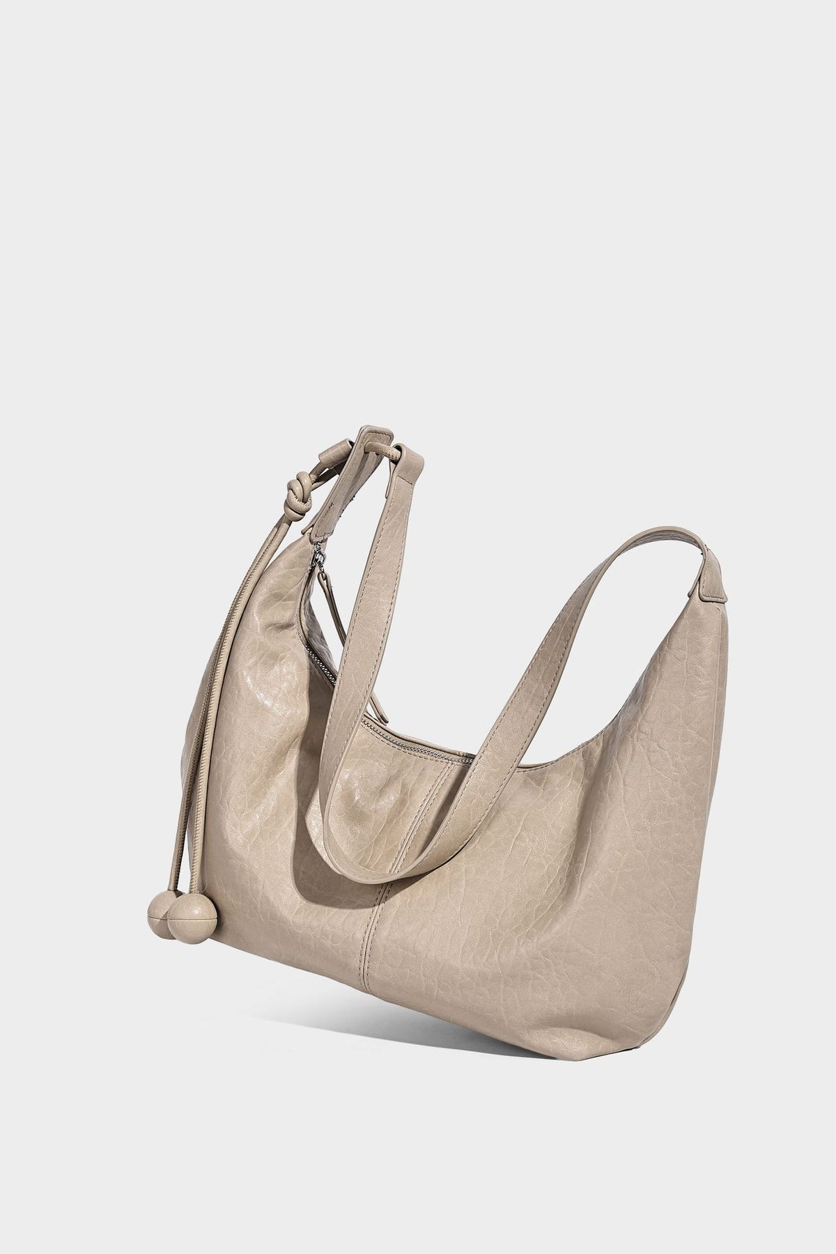 Slouchy crescent half-moon shoulder bag in pink pebbled textured finish with floral charm and knotted side detail, detail