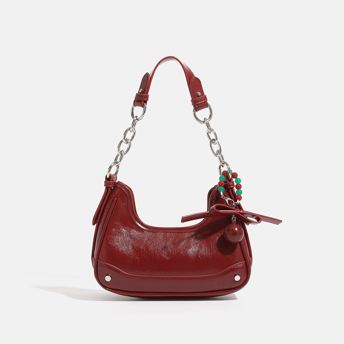 Compact crescent hobo shoulder bag in glossy burgundy leather-look finish with silver chain strap, red and green bead tassel