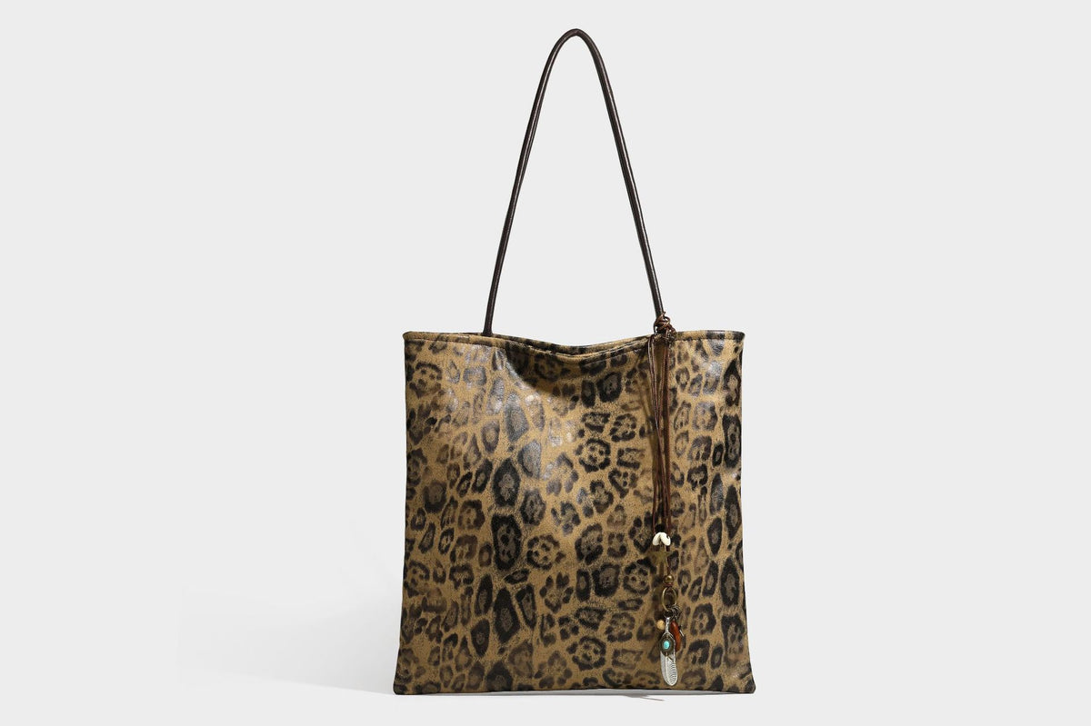 Large leopard print shoulder tote bag in tan and brown with slim dark straps and dangling beaded charm hardware, detail view