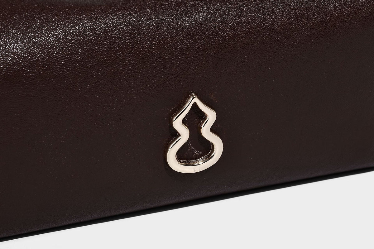 Lässig fallende, sichelförmige Hobo-Schultertasche in glatter dunkelbrauner Lederoptik mit Logo-Anhänger in Goldoptik und verstellbarem Schulterriemen