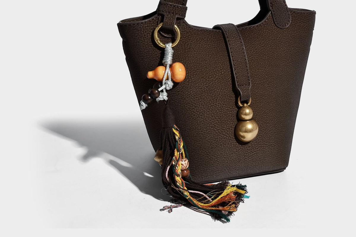 Kleine matte Beuteltasche mit genarbter Oberfläche, antikgoldfarbenen Ringbeschlägen, Perlen- und Quastenanhänger, kurzen Tragegriffen oben und