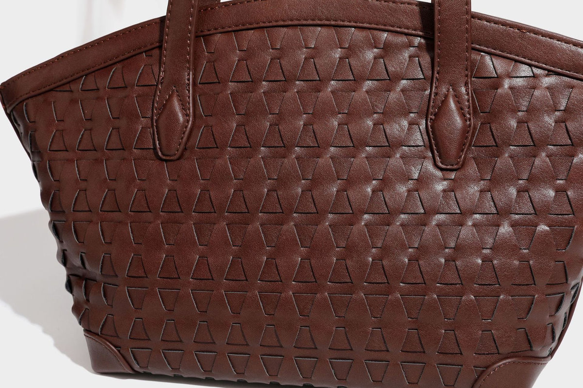 Large leather-look tote bag with geometric woven emboss, double shoulder straps, and round woven cord charm in brown, detail