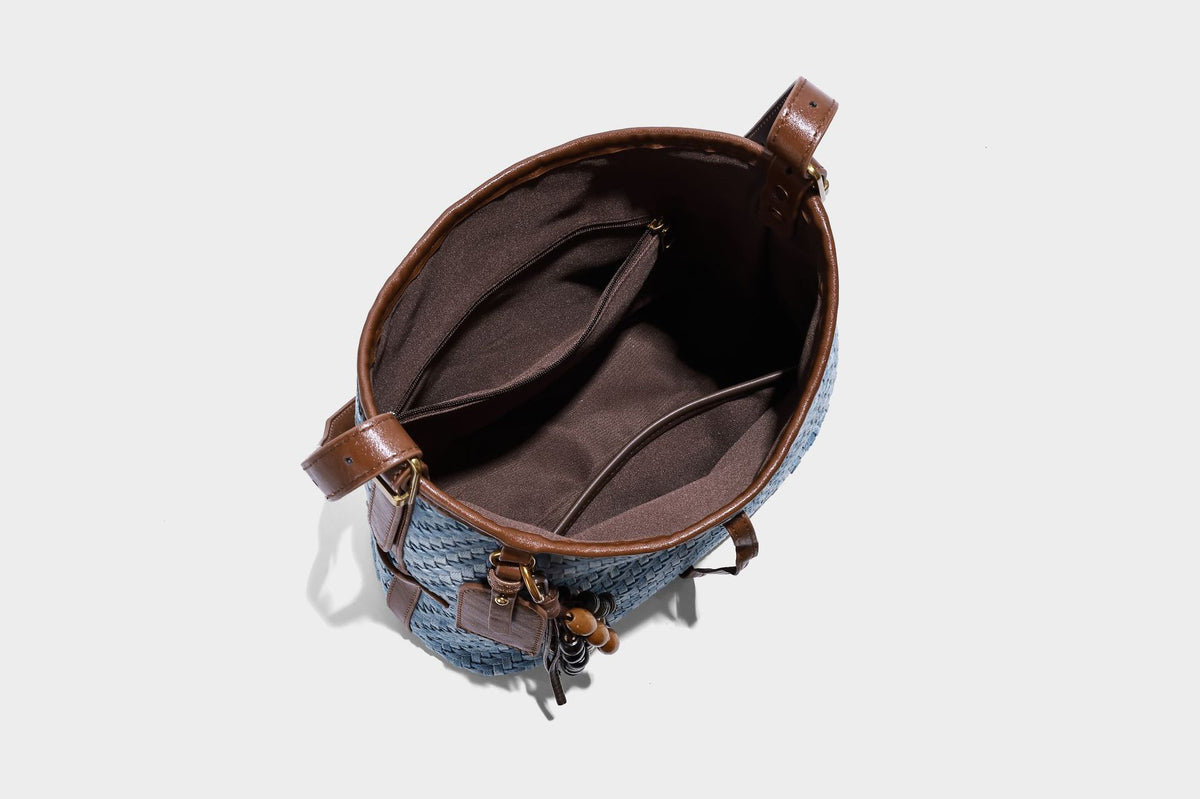 Light blue woven bucket bag with brown leather-look trim, gold-tone hardware, adjustable shoulder strap, and decorative bead