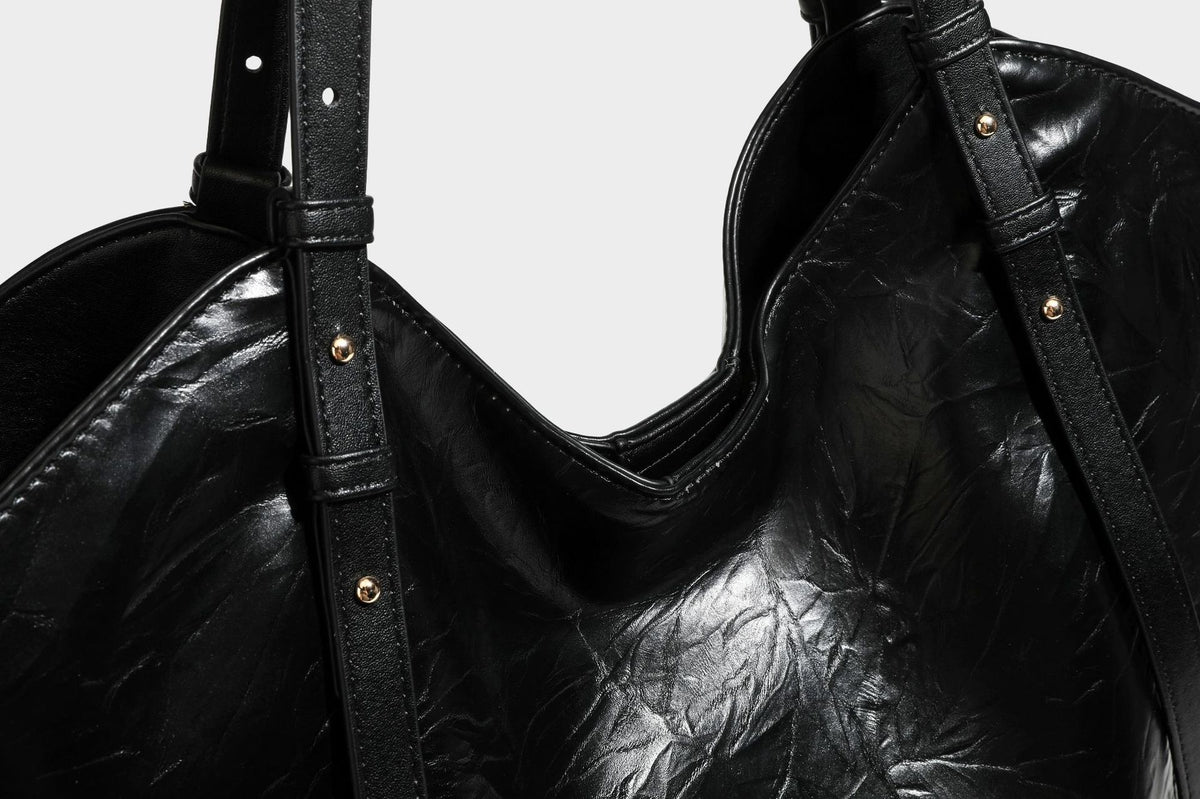 Große, glänzende Tote-Bag aus schwarzem Lederimitat mit geknitterter Optik, lässig fallender Trapezsilhouette, zwei Schulterriemen und goldfarbenen