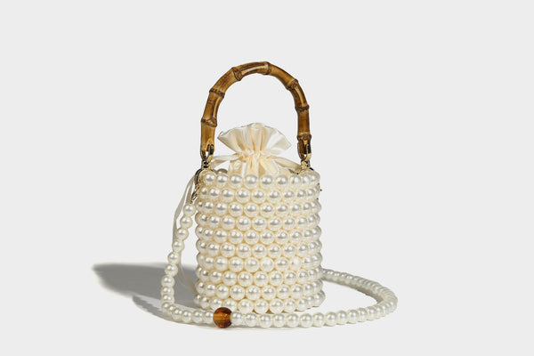 Small cylindrical bucket bag with glossy faux-pearl bead exterior, bamboo arched top handle, satin drawstring closure, and