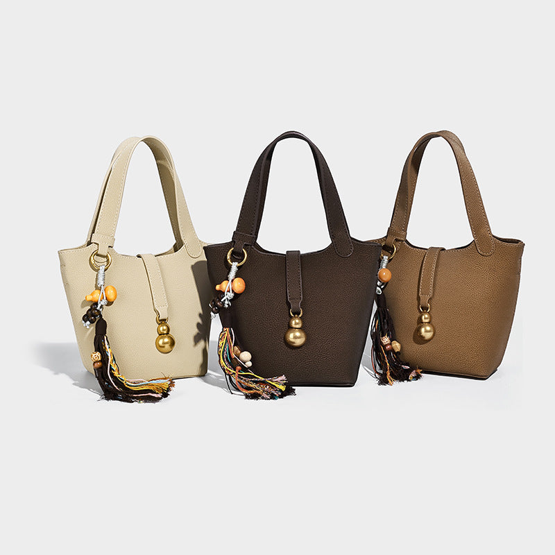 Small pebbled matte bucket bag with antique gold-tone ring hardware, bead-and-tassel charm, short top handles, and