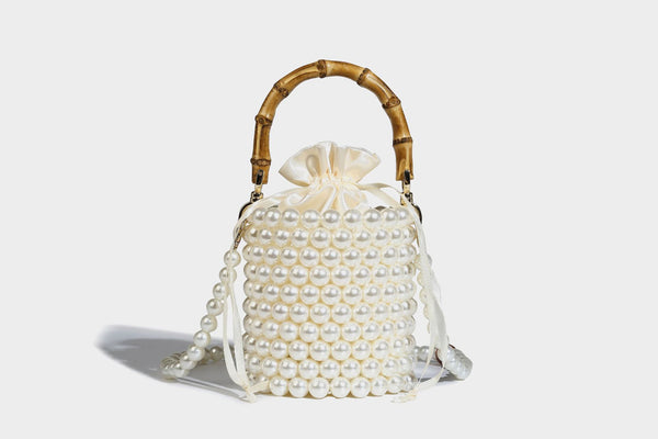 Small cylindrical bucket bag with glossy faux-pearl bead exterior, bamboo arched top handle, satin drawstring closure, and