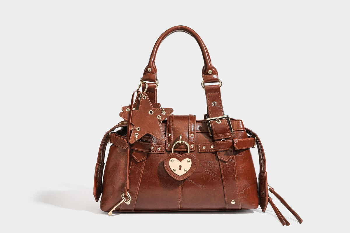 Structured leather-look satchel bag with heart padlock charm, star charm, gold-tone buckle hardware, dual top handles, and