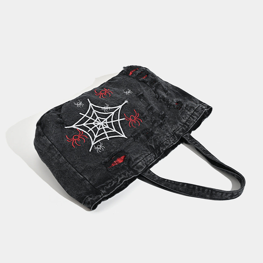 Large washed black distressed denim tote bag with white spider web embroidery and red spider motifs on the front panel