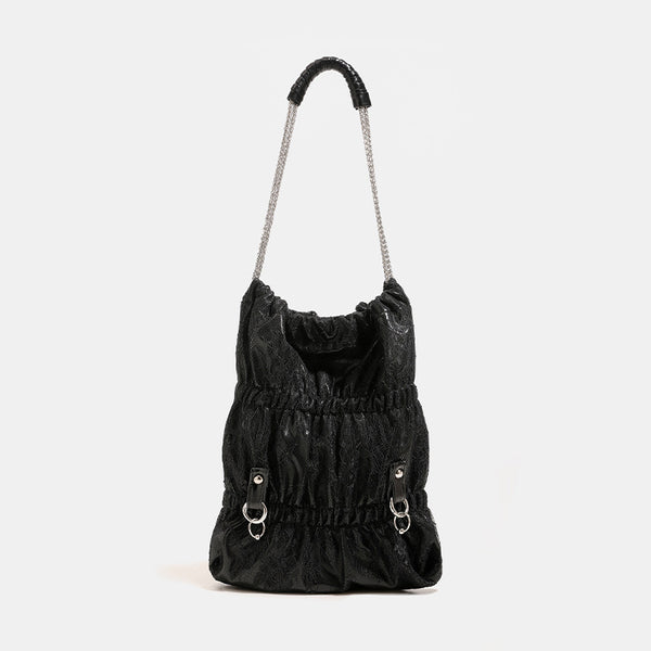 Slouchy lace-overlay bucket bag with silver chain strap, draped chain detail, shell charms, and drawstring top closure
