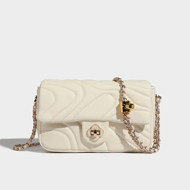 Compact cream quilted flap crossbody bag with wave stitching, gold-tone chain strap, and four-petal turn-lock clasp, detail