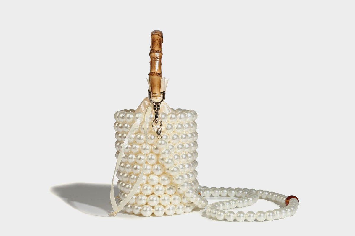 Small cylindrical bucket bag with glossy faux-pearl bead exterior, bamboo arched top handle, satin drawstring closure, and