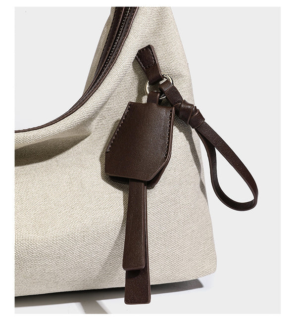 Cream canvas hobo shoulder bag with dark brown leather-look trim, zip-top closure, adjustable strap, and silver-tone