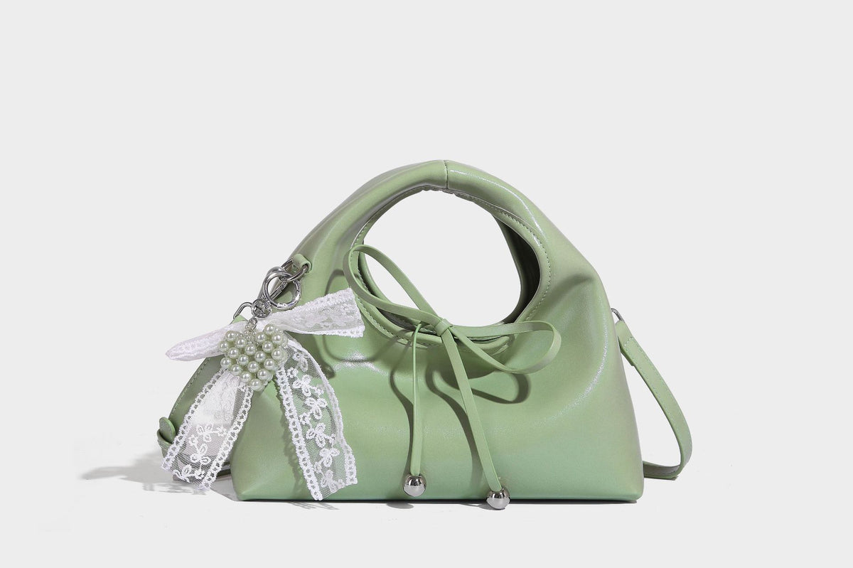Kleine kuppelförmige Henkeltasche in glänzender Lederoptik mit Kordelzugverschluss, weißem Spitzen-Schleifenanhänger und silberfarbenen Metallbeschlägen