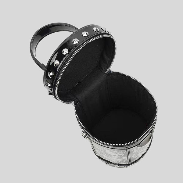 Black glossy cylindrical barrel bag with white skull-floral print panels, silver pyramid studs, black beaded top handle, and